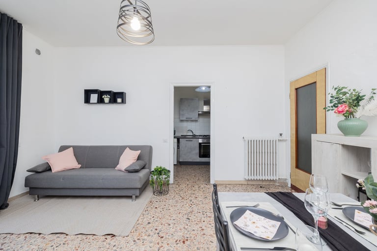 Modern studio apartment interior with gray sofa, open kitchen, wooden door, and living space with dining area
